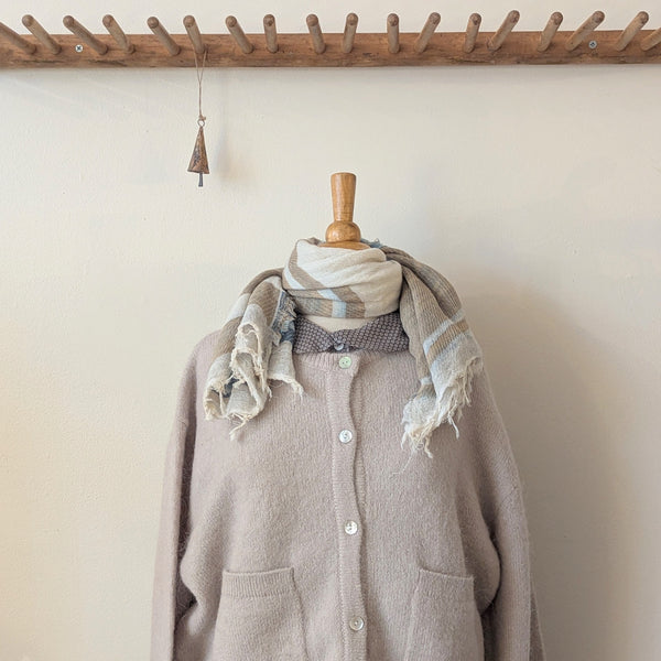 Mannequin wearing a beige cardigan with a scarf and tie against a plain wall.