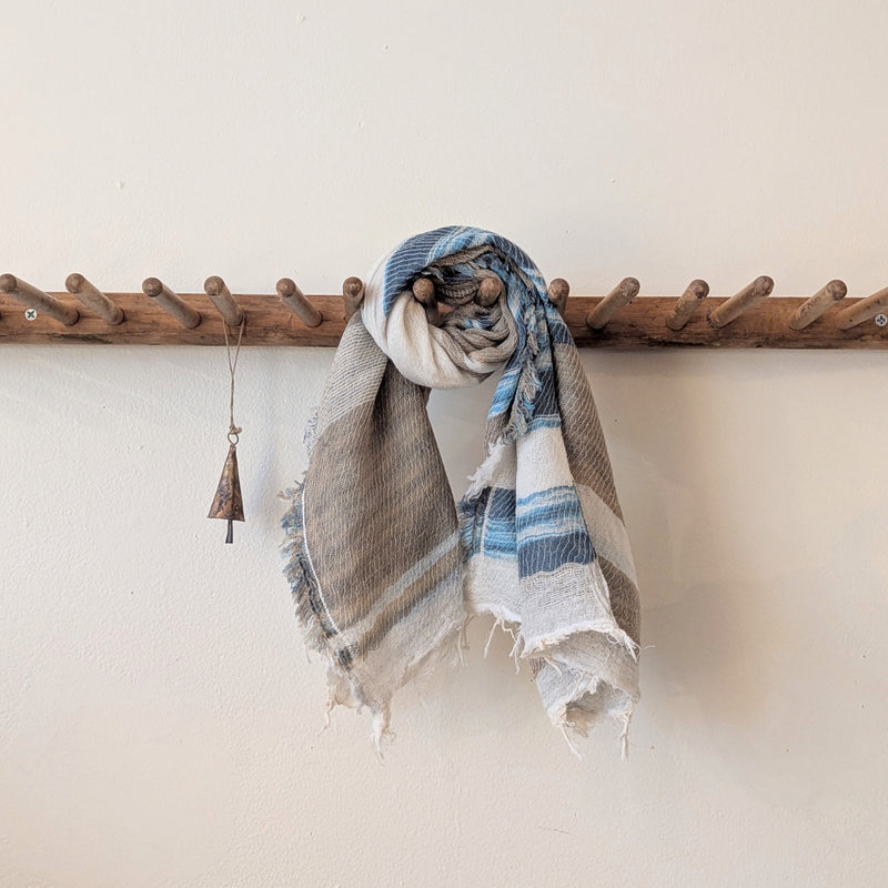 Textured scarf draped over a wooden coat rack against a white wall.