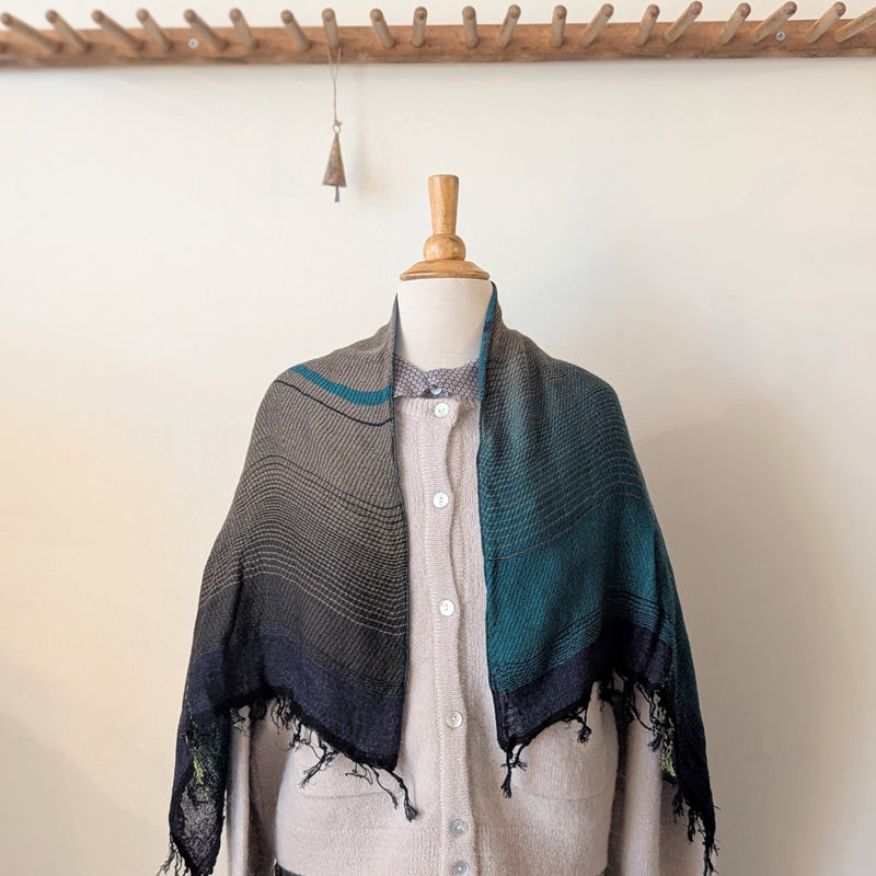 Mannequin wearing a gray and green knitted shawl with a beige cardigan against a neutral background.