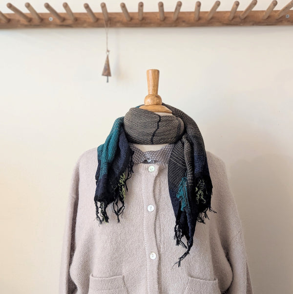 Mannequin wearing a beige cardigan with a patterned scarf against a plain wall.