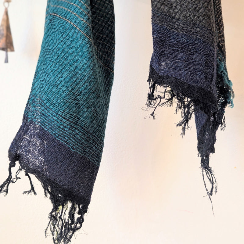 Two woven scarves with fringes, one blue and one black, on a neutral background.
