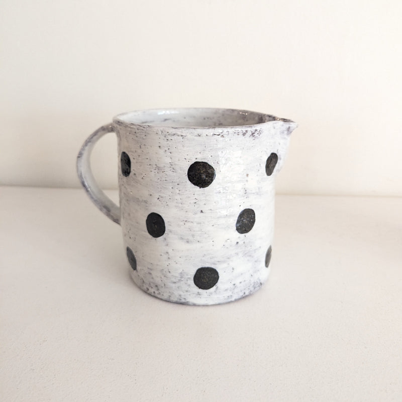 White ceramic pitcher with black speckles on a beige background