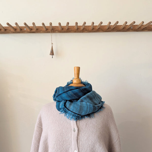 Blue scarf draped over a mannequin wearing a beige sweater against a neutral background