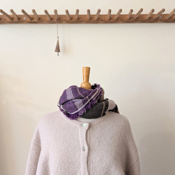 Mannequin wearing a purple and gray checkered scarf with a wooden hook and decorative object in the background.