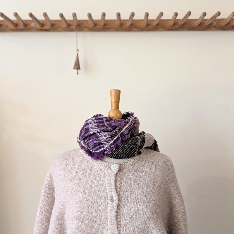Mannequin wearing a purple and gray checkered scarf with a wooden hook and decorative object in the background.