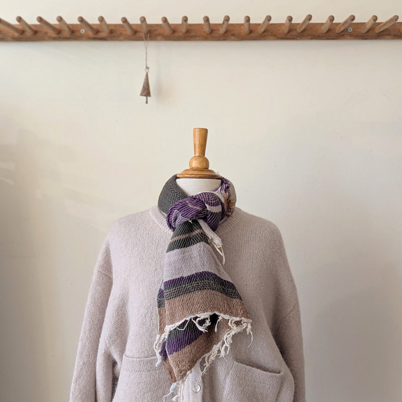 Mannequin wearing a light gray sweater with a plaid scarf draped over it, against a plain wall.