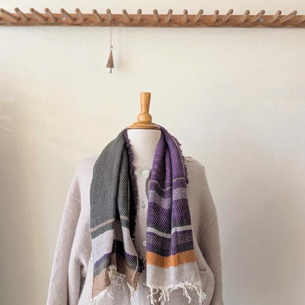 Mannequin wearing a gray sweater with a purple and orange striped scarf against a white wall.