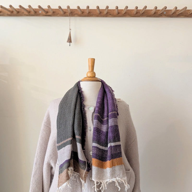 Mannequin wearing a gray sweater with a purple and orange striped scarf against a white wall.