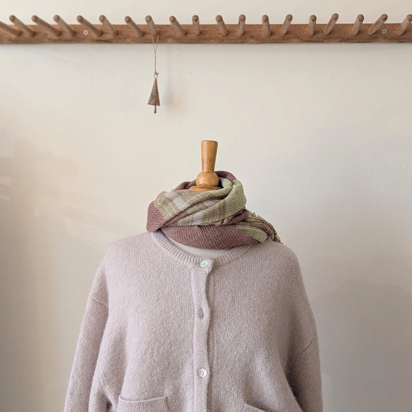 Mannequin wearing a light pink cardigan with a patterned scarf, against a neutral background.