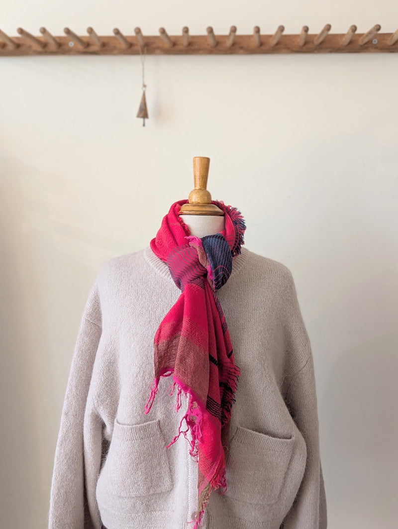 Mannequin wearing a pink and purple scarf with a beige sweater against a white wall.