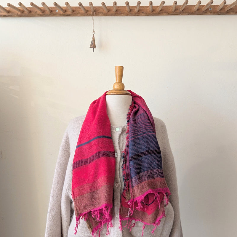 Mannequin wearing a pink and purple striped scarf with a wooden hook in the background.