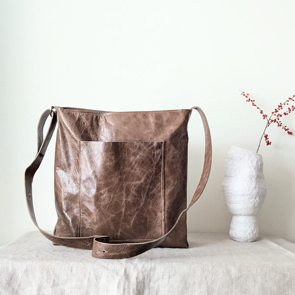 Brown leather bag on a white surface with a vase and branches in the background