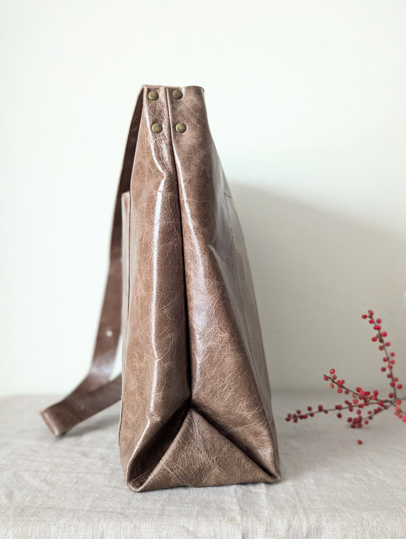 Brown leather tote bag on a light surface with a minimal background