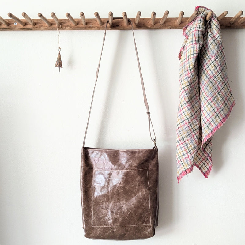 Brown leather bag hanging on a wooden rack with a plaid towel in the background.