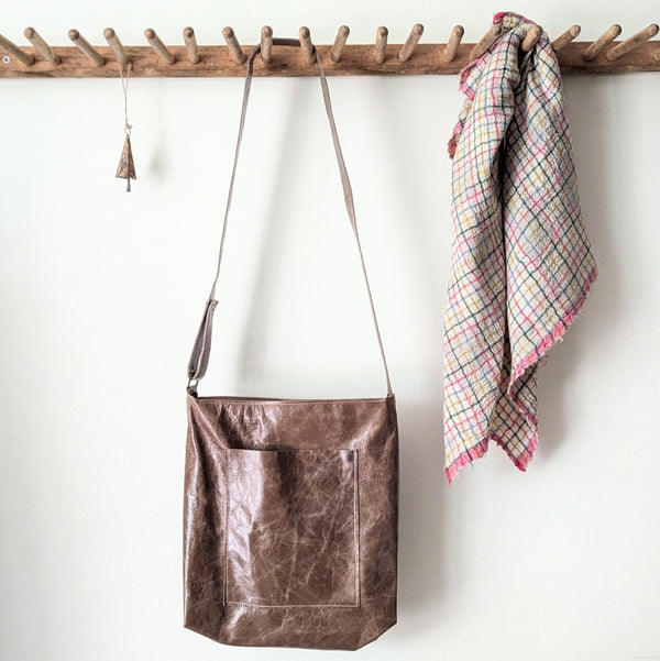 Brown leather bag hanging on a wooden rack with a plaid towel next to it.