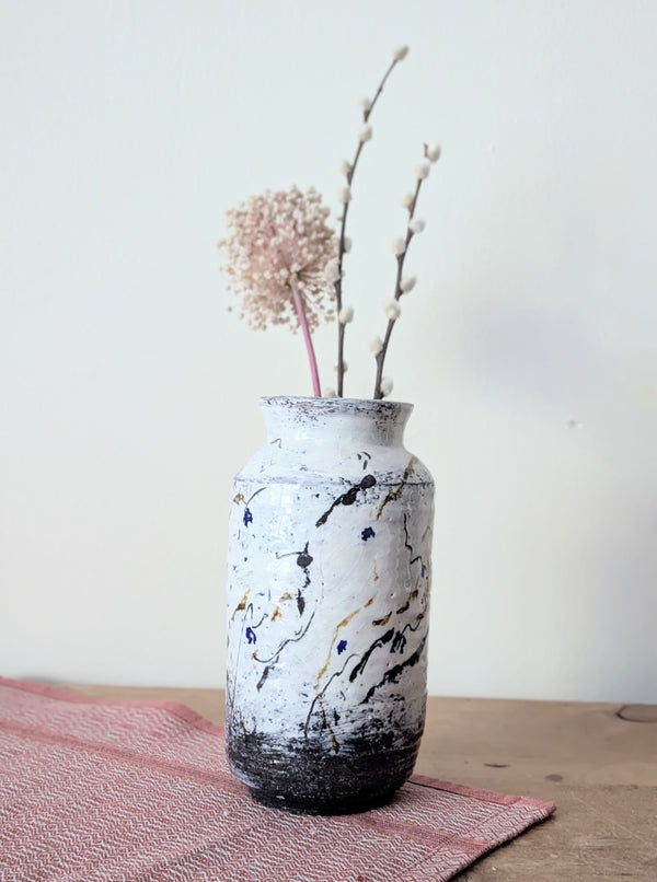 White vase with black marbled pattern on a wooden surface with a pink textured cloth