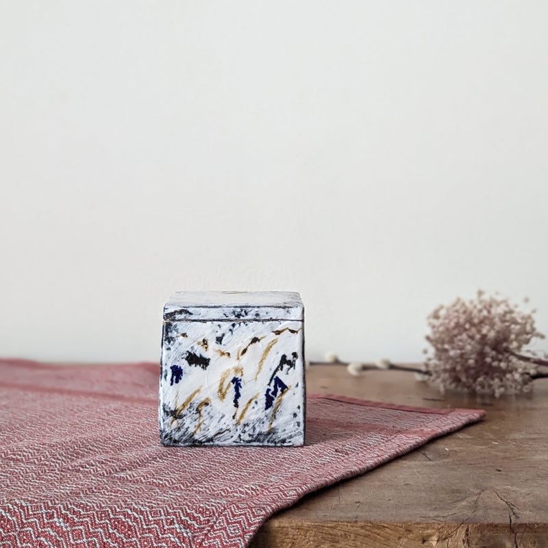Marble-patterned cube on a wooden surface with a pink textured cloth and dried flowers in the background