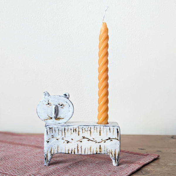 Decorative cat candle holder with a twisted orange candle on a wooden surface.