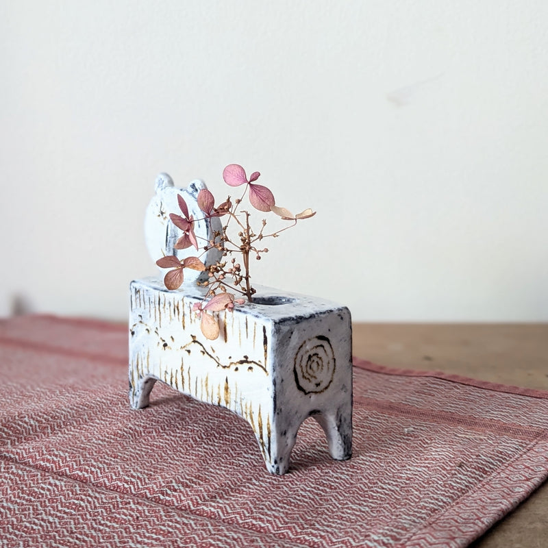 Small ceramic cat candle holder with dried flowers on a textured surface