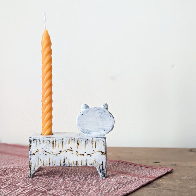 Cat-shaped candle holder with a twisted orange candle on a wooden surface.