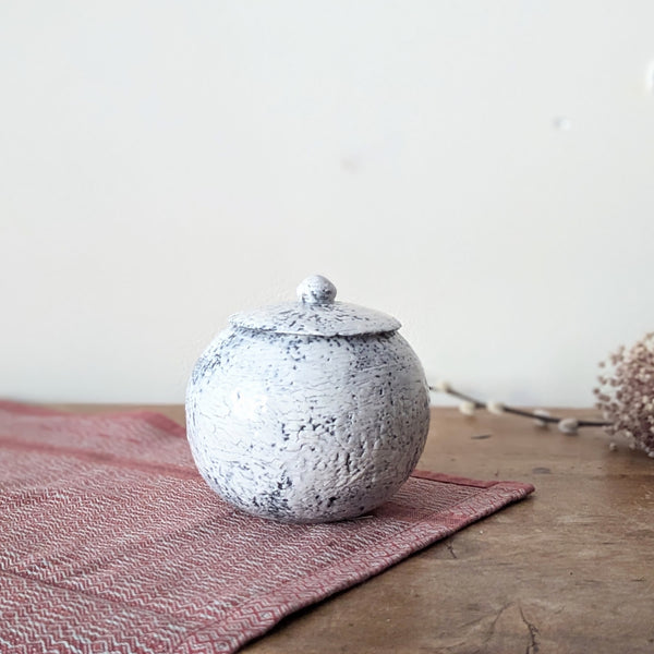 Speckled ceramic jar on a pink textured mat with a neutral background