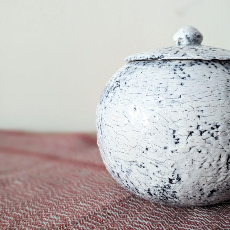 Speckled ceramic jar with lid on a textured surface