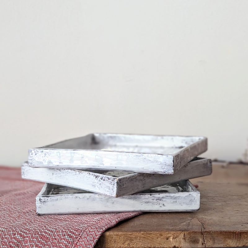 Stack of three rectangular ceramic  trays with a rustic finish on a wooden surface.