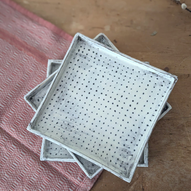 Stack of ceramic trays with perforated design on a wooden surface