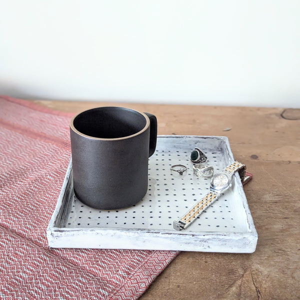 Black mug on a decorative ceramic tray with jewelry on a wooden surface