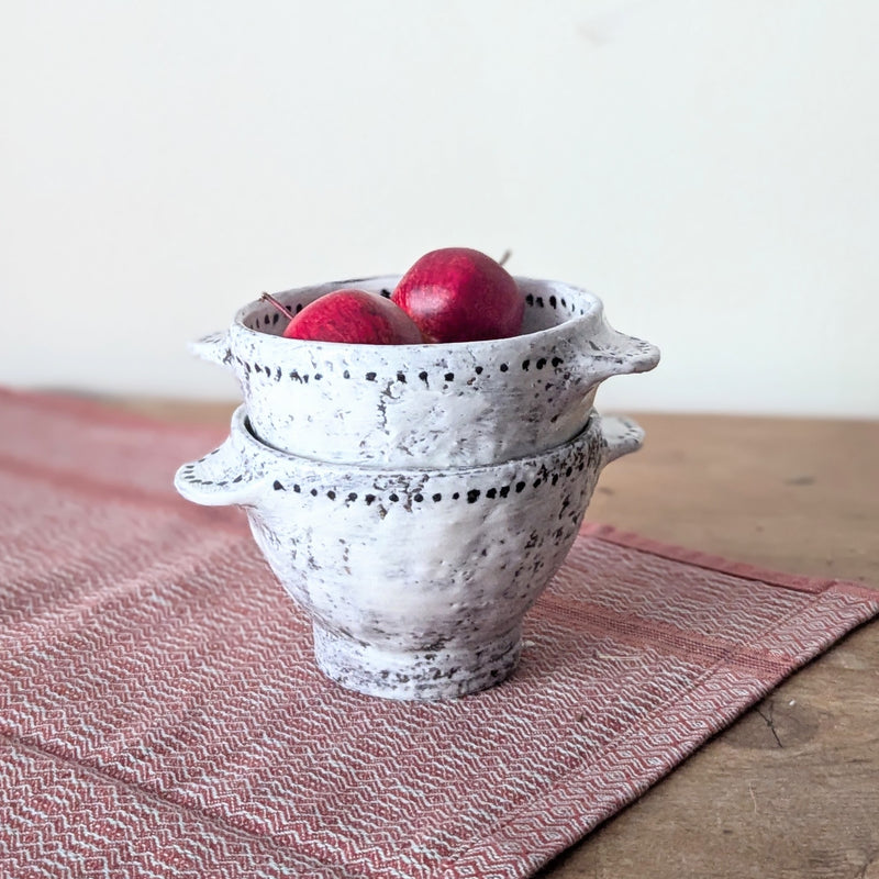 Stack of ceramic bowls with apples on a wooden surface