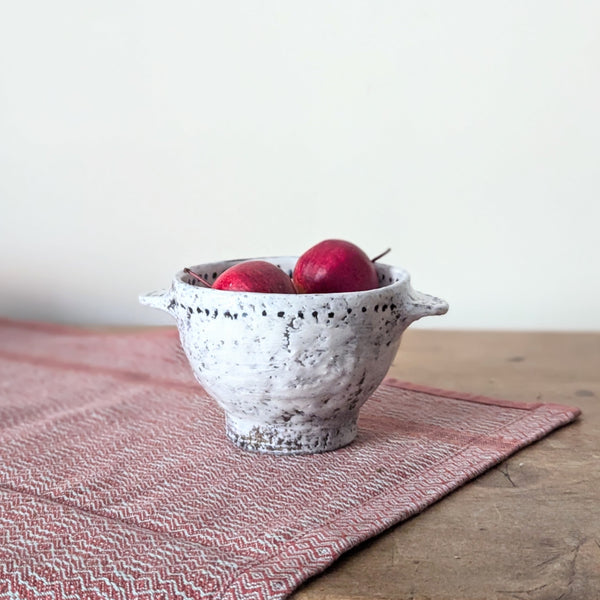 White textured ceramic bowl with apples on a wooden table and pink cloth