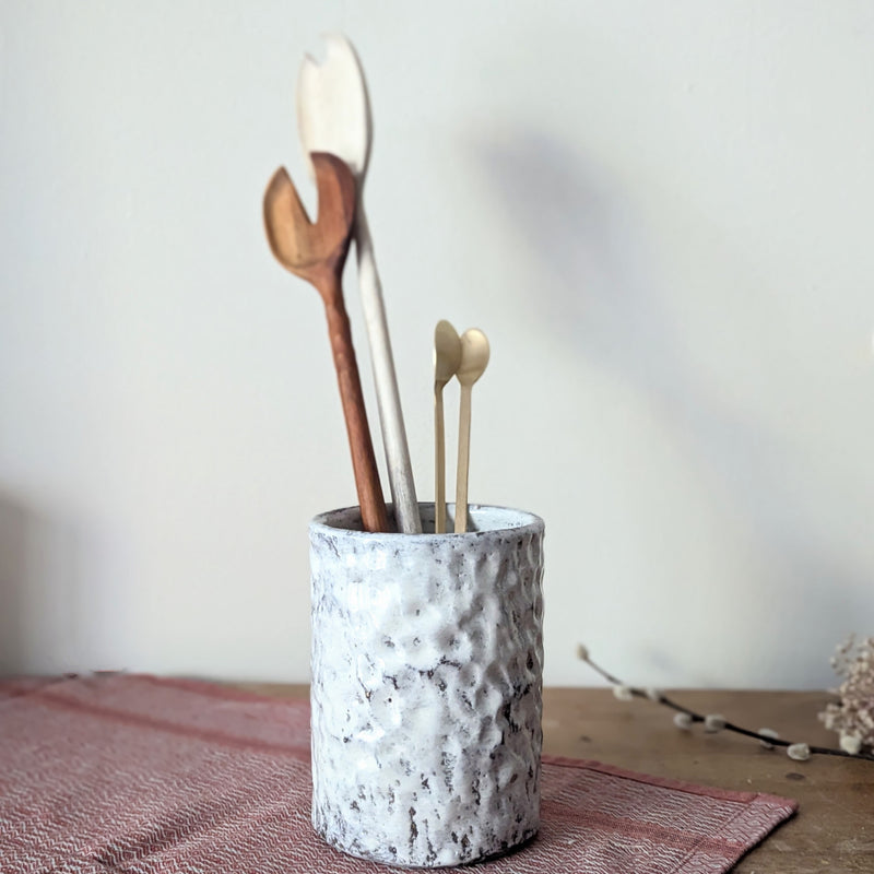 Ceramic holder with wooden utensils on a neutral background