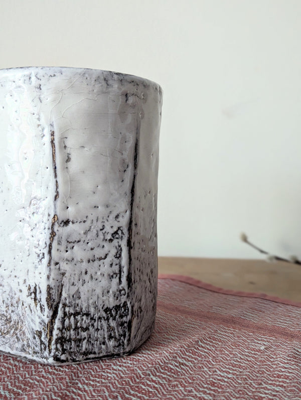 Textured ceramic vase on a textured surface with a neutral background