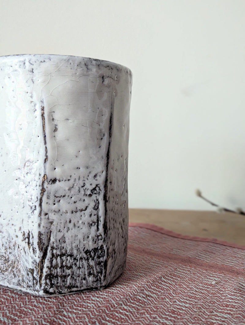 Textured ceramic vase on a textured surface with a neutral background