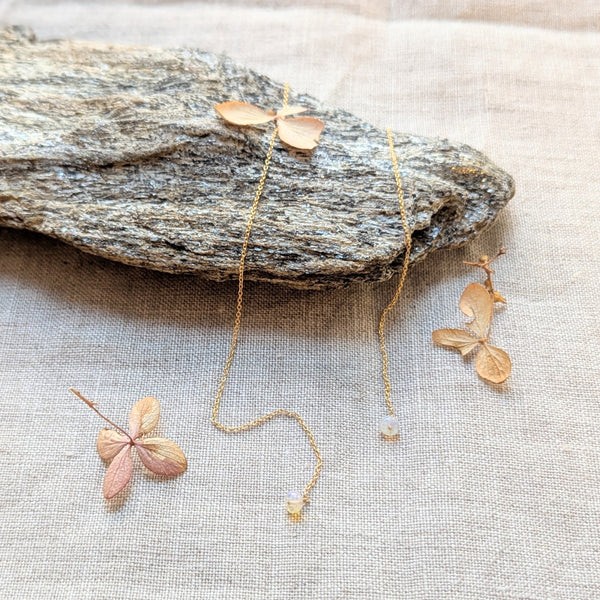 Delicate gold thread earring with opal pendants on a stone surface
