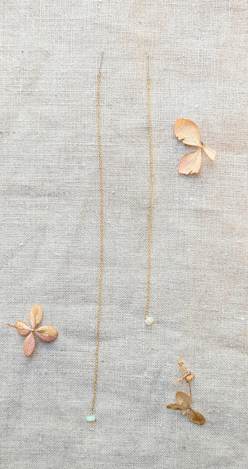 Delicate gold thread earring with opal pendants on a stone surface