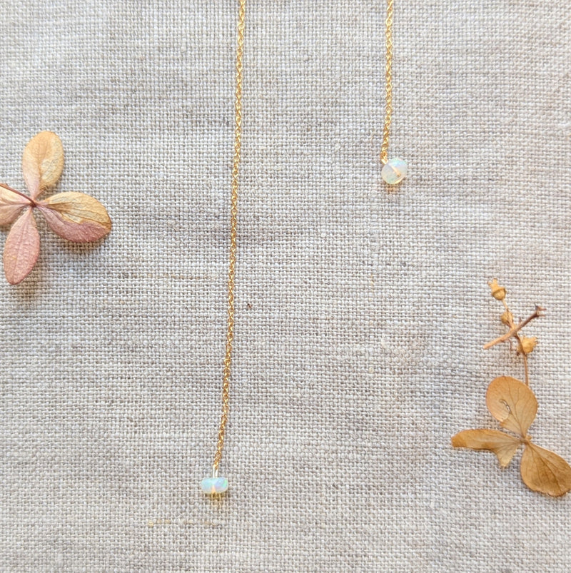 Delicate gold thread earring with opal pendants on a linen surface