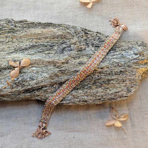 Bracelet with orange blue pink and grey string woven in on a textured surface