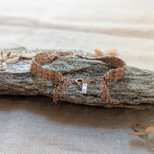 Bracelet with orange blue pink and grey string woven in with a clasp on a textured surface