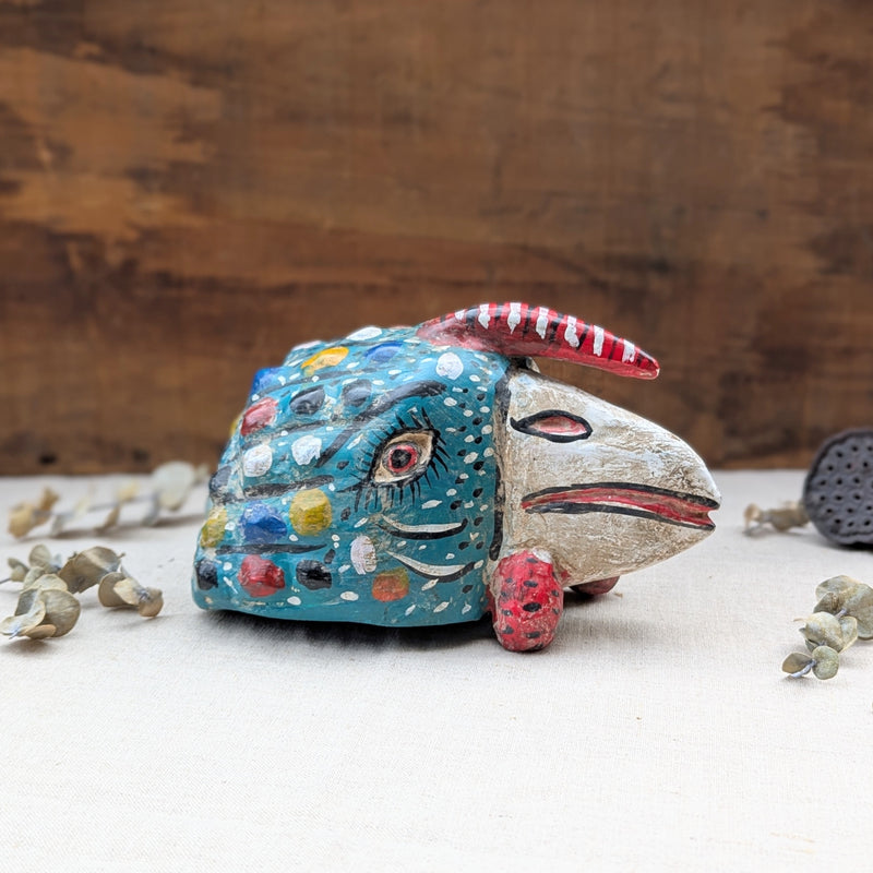 side view of a blue wooden rooster mask on a neutral background.