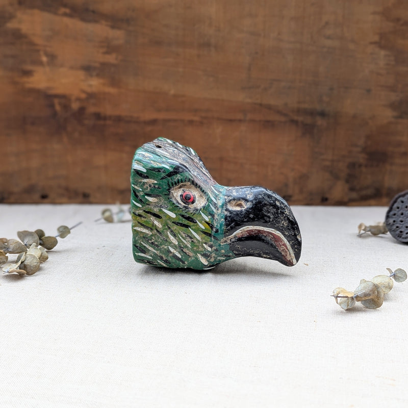 side view of a green wooden bird mask on a neutral background.