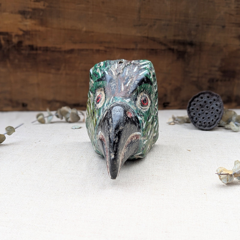 front view of a green wooden bird mask on a neutral background.