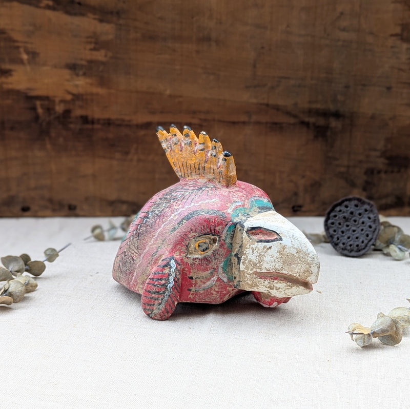 front view of a red wooden rooster mask on a neutral background.