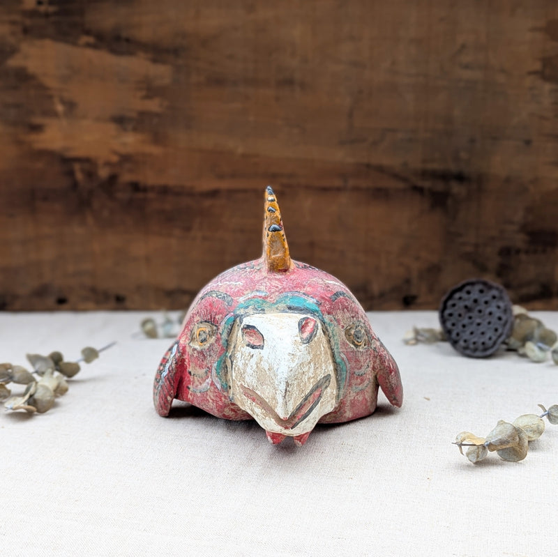 front view of a red wooden rooster mask on a neutral background.