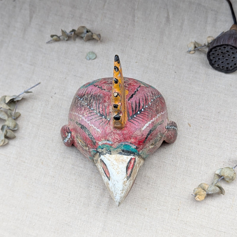 top view of a red wooden rooster mask on a neutral background.