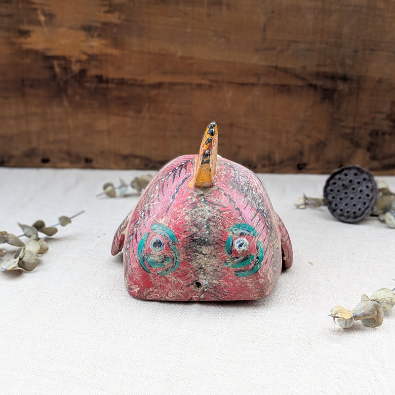 back view of a red wooden rooster mask on a neutral background.