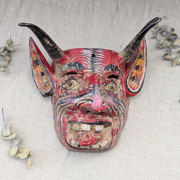 front view of a red wooden devil mask on a neutral background