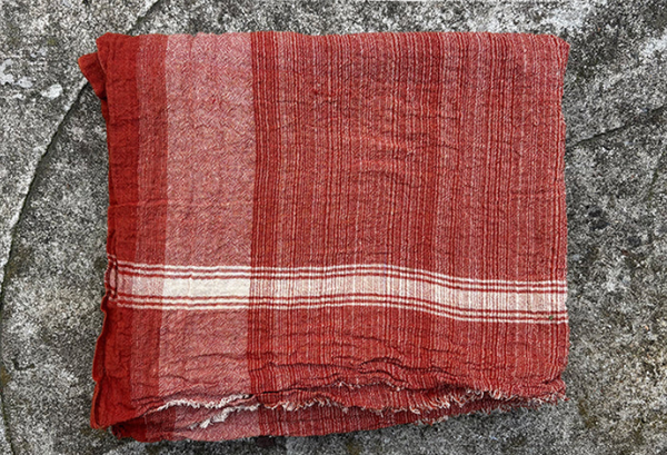 Folded rust colored towel with white stripes on a textured gray surface