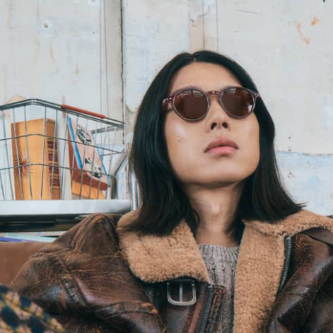 Person wearing brown sunglasses and a brown leather jacket in an urban setting
