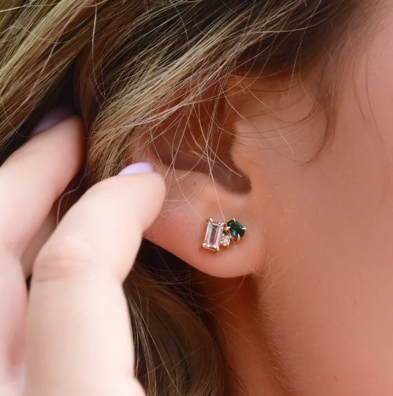 Close-up of an ear wearing a gold earring with green gemstones, with a hand adjusting hair.